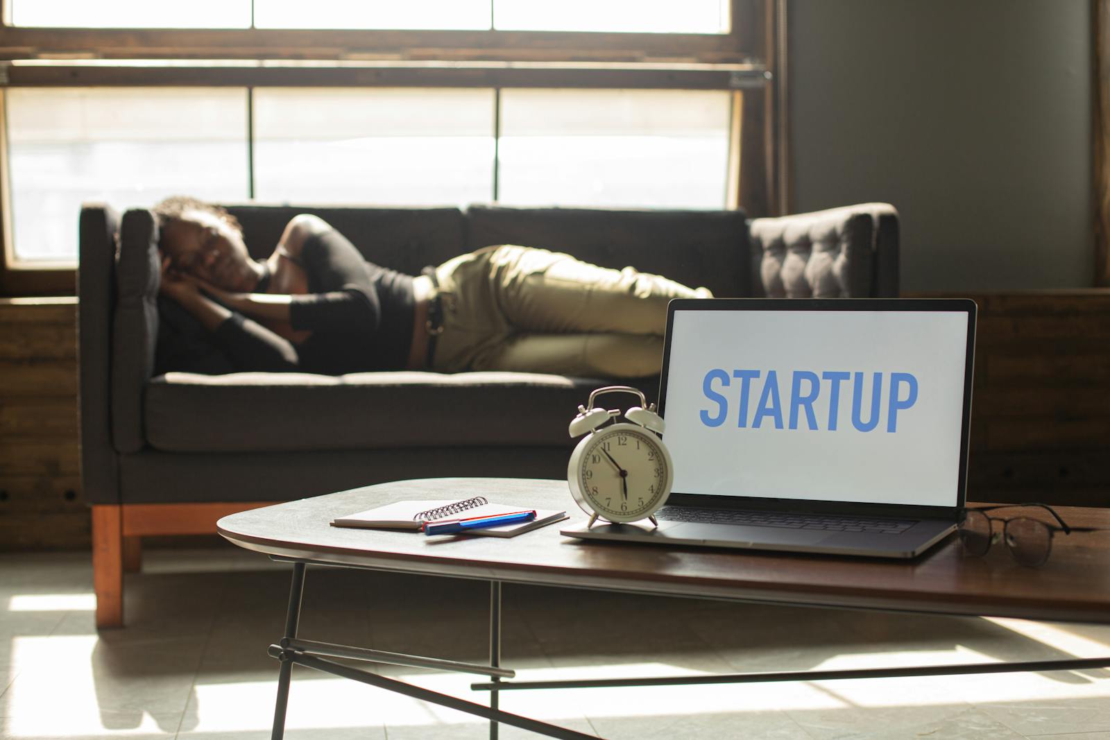 A woman lies on a sofa while a laptop displays 'STARTUP,' capturing a workspace vibe.